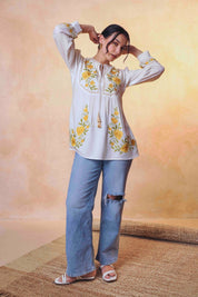 indigrey Goa white top with yellow floral tatami embroidery on yoke and sleeves worn by a model with blue jeans.