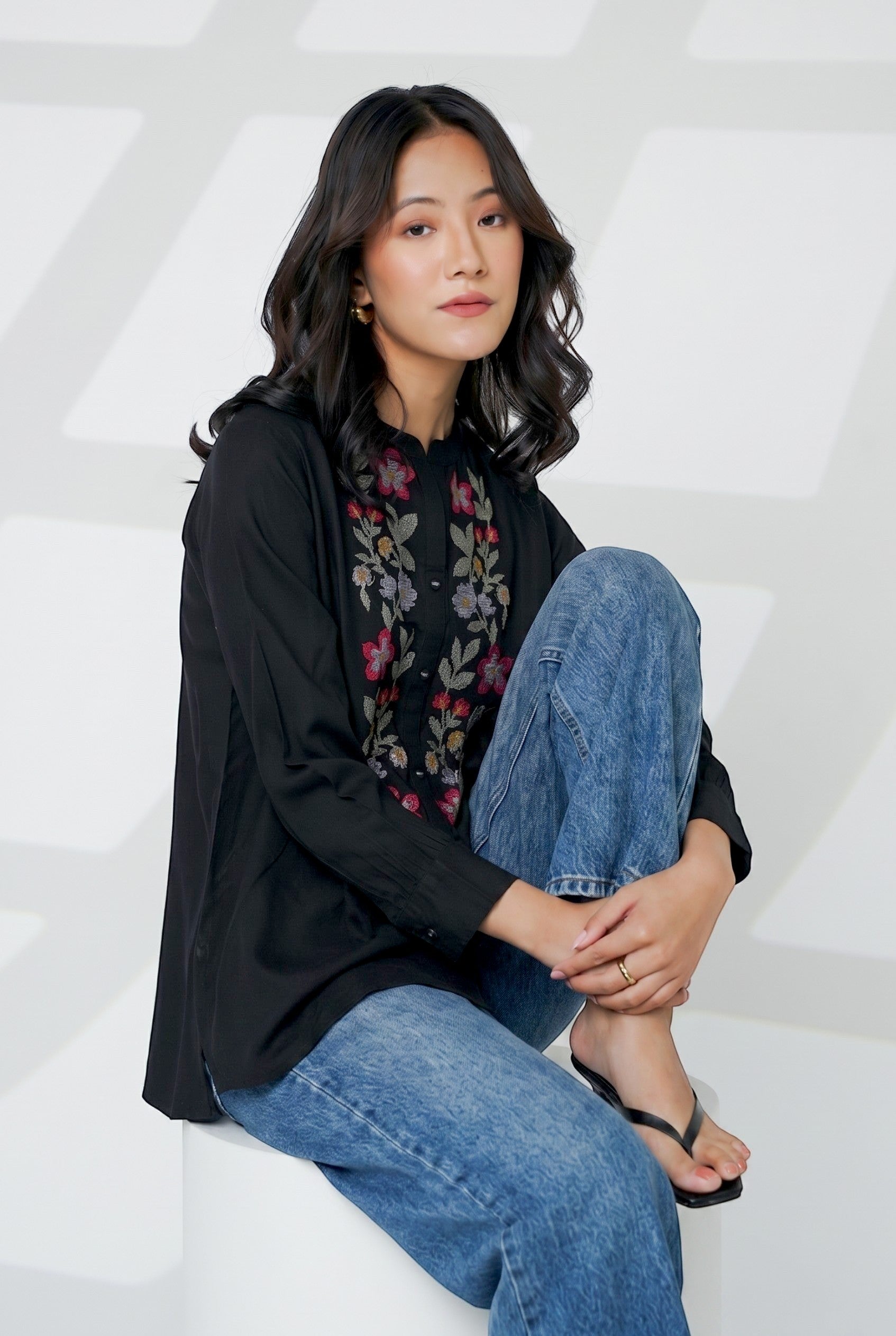 indigrey Aurora black shirt featuring handcrafted cross stitch floral embroidery worn by a woman with blue jeans