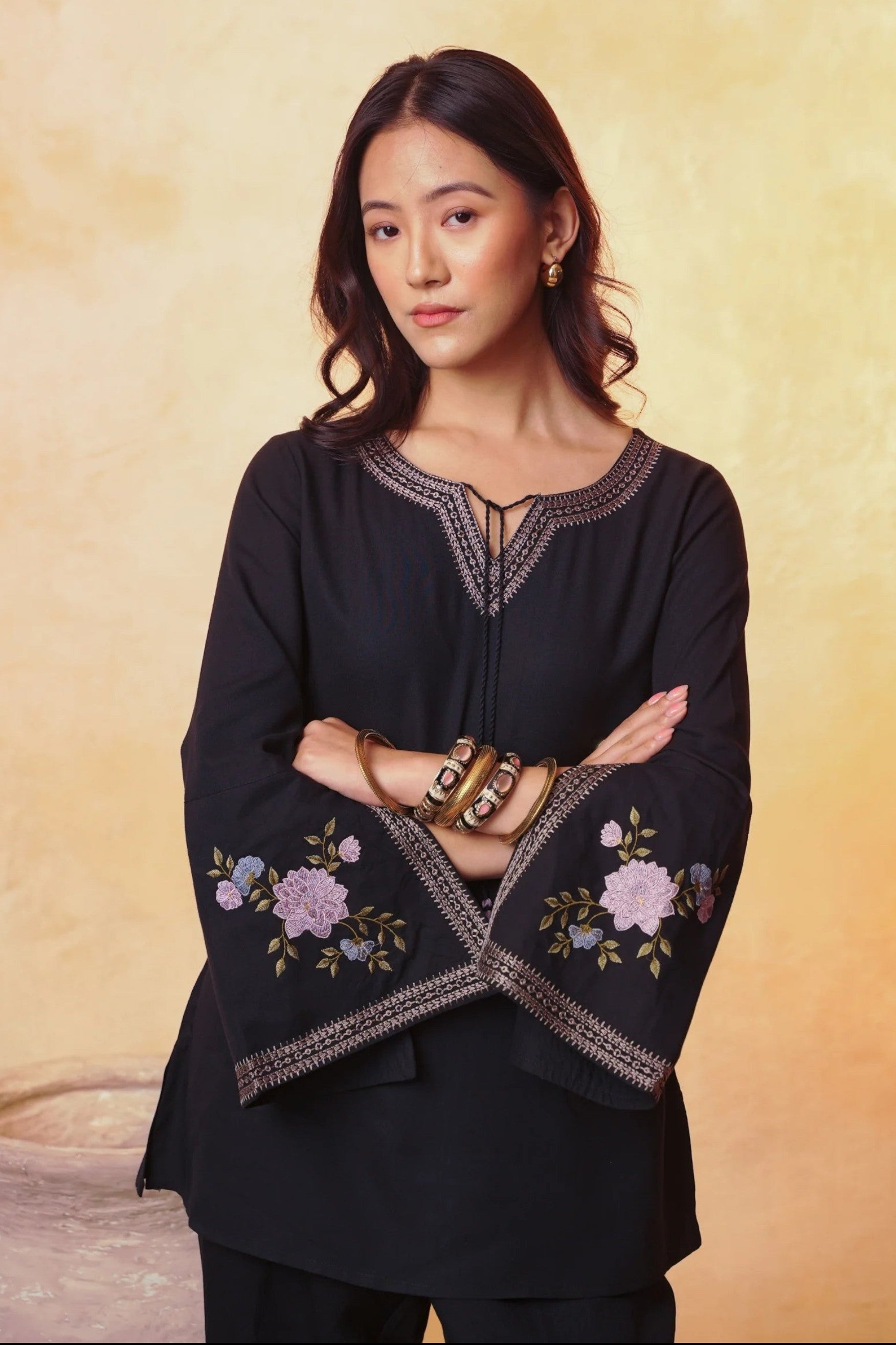 Model wearing an indigrey black viscose top with floral embroidery on flared bell sleeves and tassel neck detail.