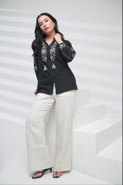 indigrey black shirt with floral embroidery on neckline and sleeves, worn by a woman with white trousers