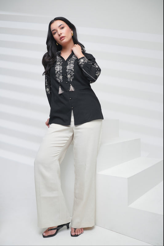 indigrey black shirt with floral embroidery on neckline and sleeves, worn by a woman with white trousers