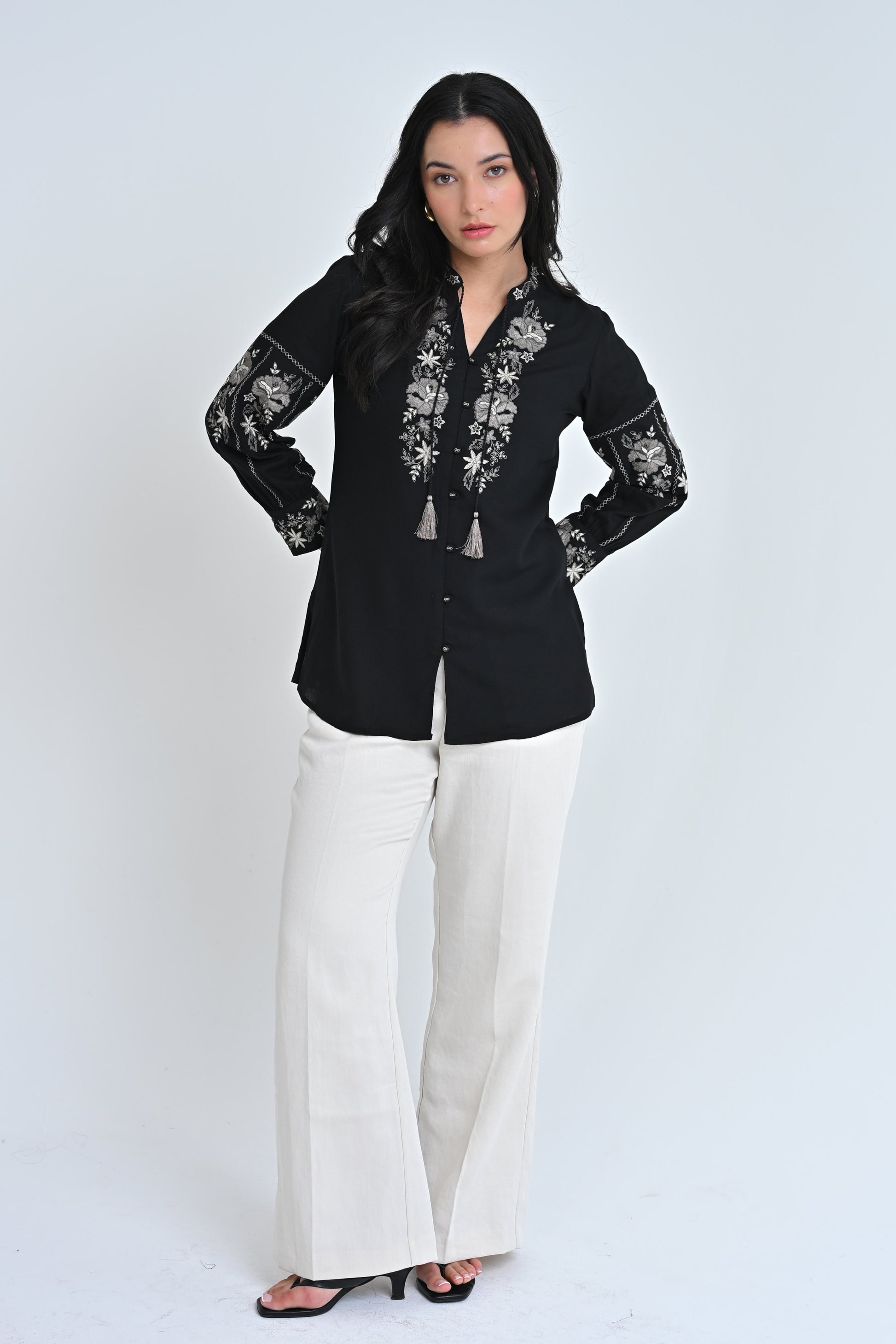 Model wearing an indigrey black shirt with intricate floral embroidery on the neckline and sleeves and tassel ties.