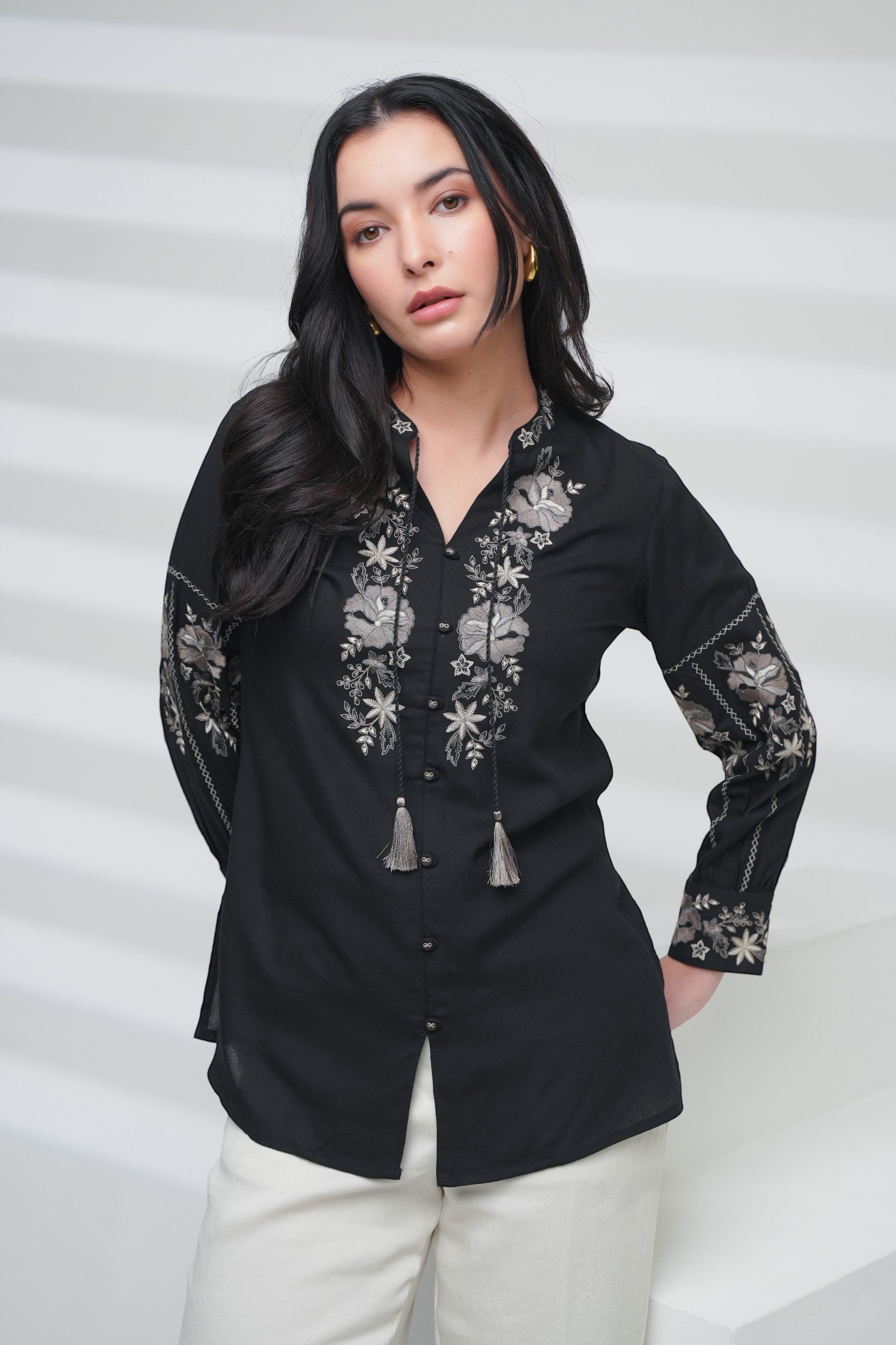 Model wearing an indigrey black shirt with intricate floral embroidery on the neckline and sleeves and tassel ties.
