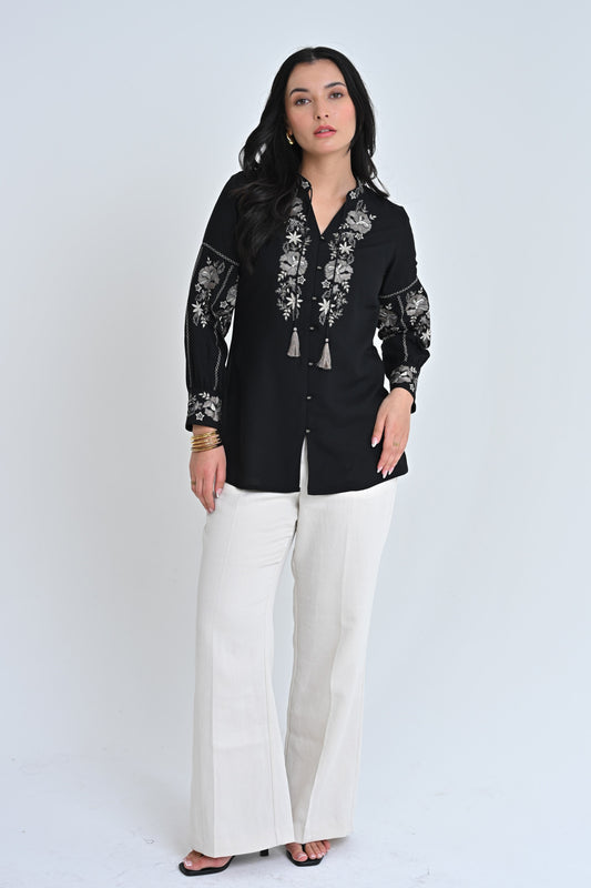 A model wearing an indigrey black shirt with intricate floral embroidery on the neckline and sleeves.