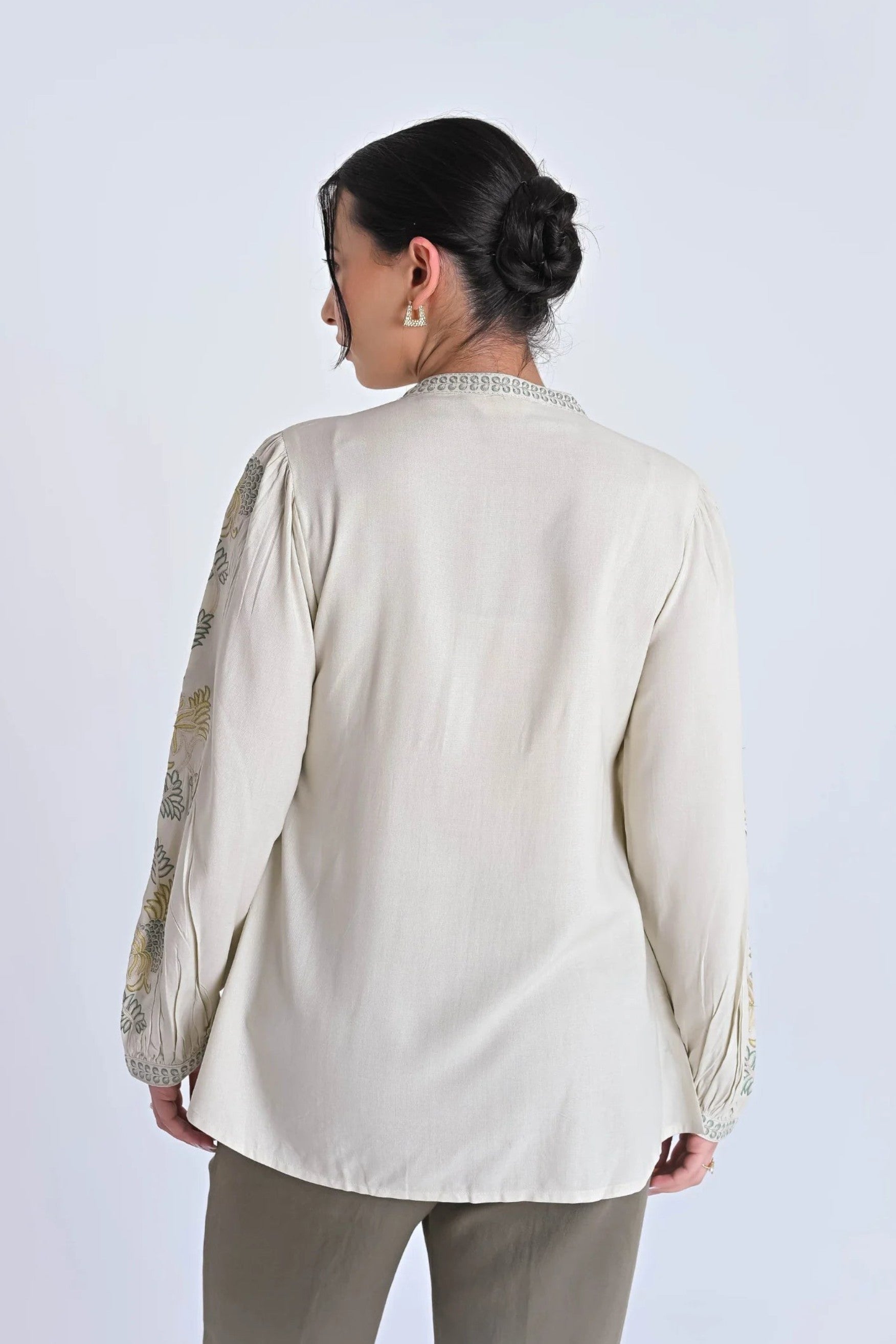 Back view of indigrey ivory Dahlia top featuring tonal pebblework embroidery on sleeves and yoke, worn with trousers.