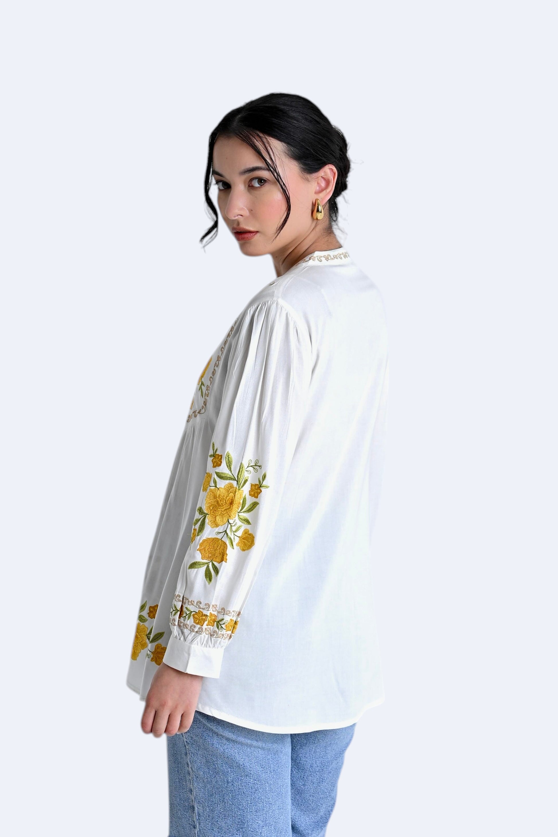 indigrey Goa white top featuring yellow floral Tatami gradient embroidery on the yoke and sleeves, worn with jeans.