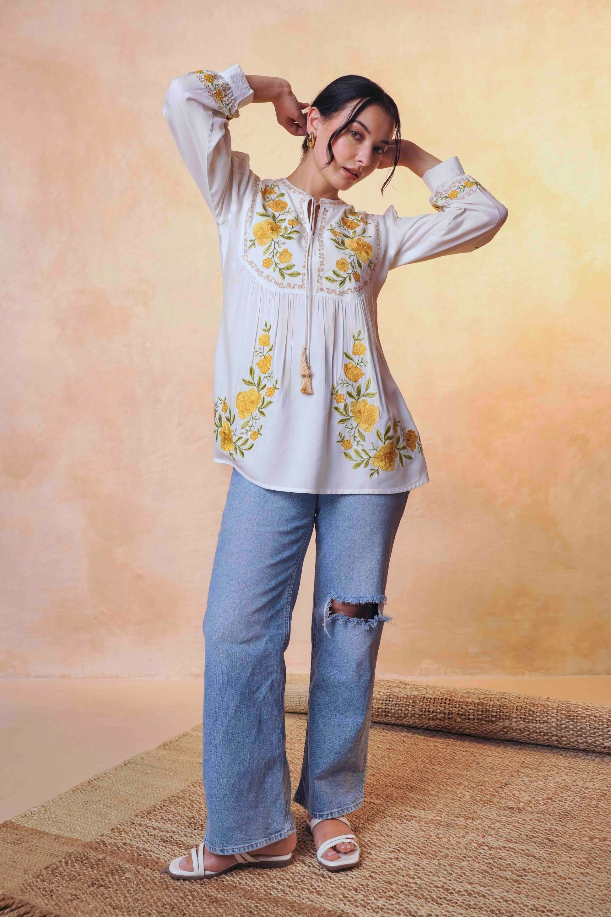 indigrey Goa white top with yellow floral tatami embroidery on yoke and sleeves worn by a model with blue jeans.