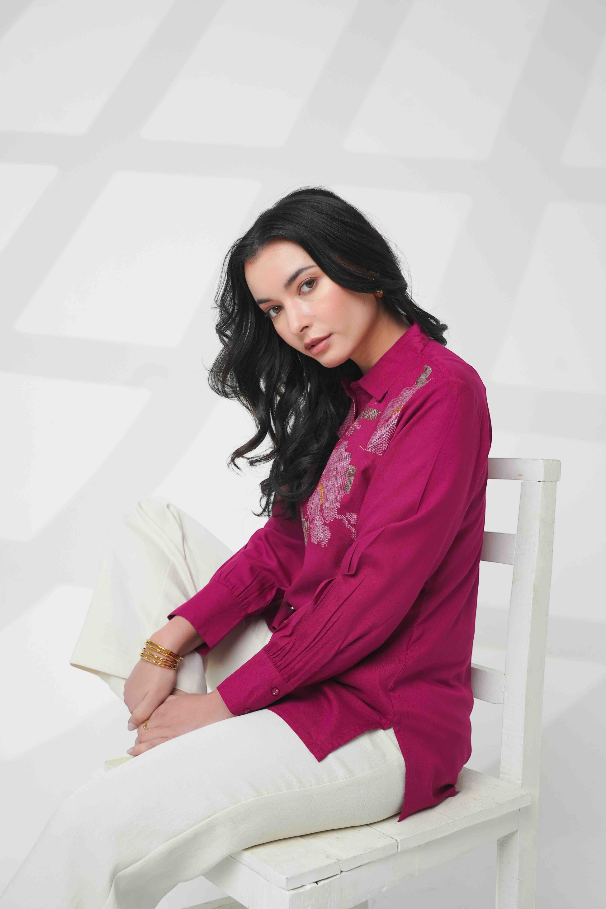 indigrey magenta long sleeve button down shirt with floral chest embroidery worn by a woman sitting on a white chair