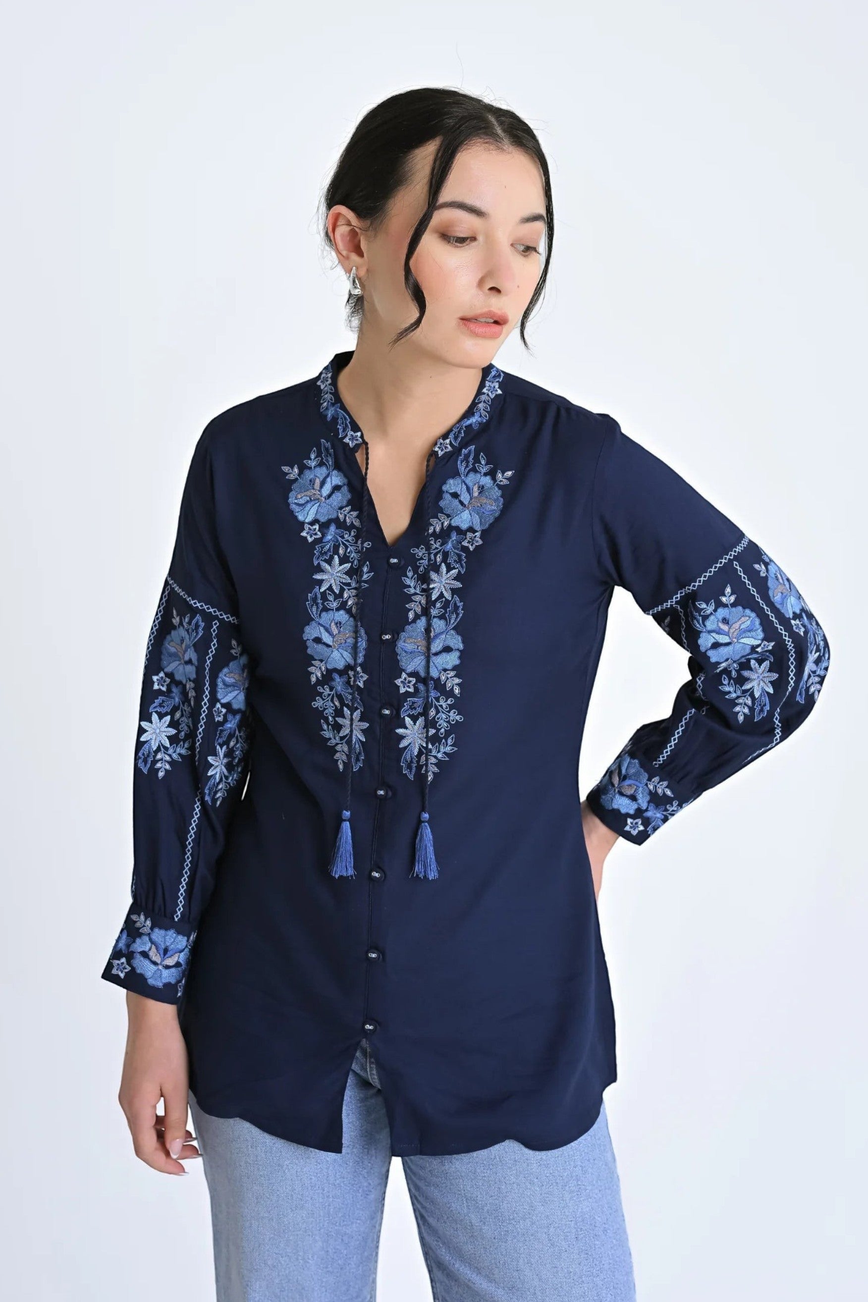 A woman wearing an indigrey navy shirt with light blue floral embroidery on the neckline and sleeves and tassel ties.