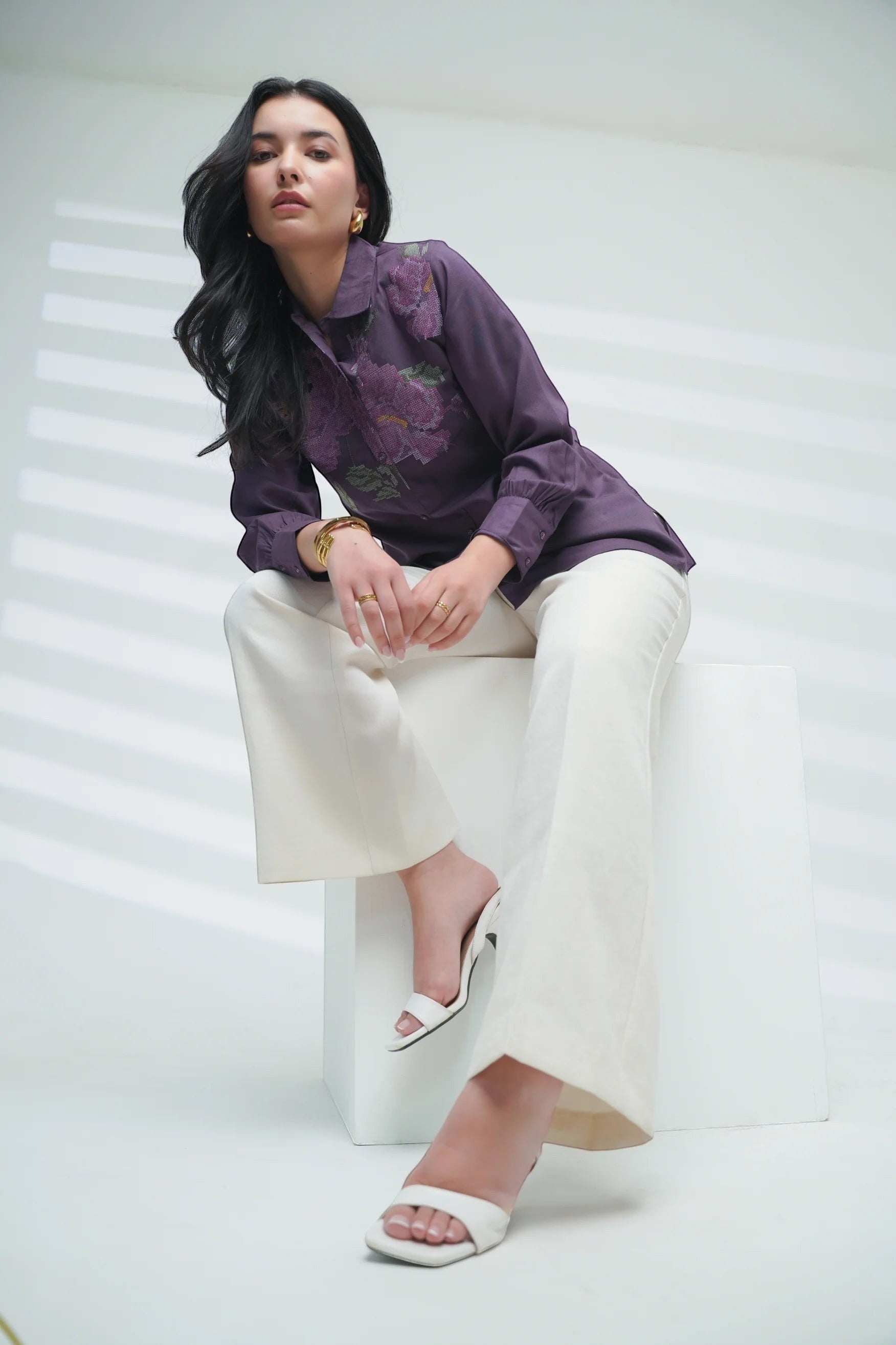 Indigrey purple shirt featuring pixel cross stitch floral embroidery, worn by a model sitting on a white block.