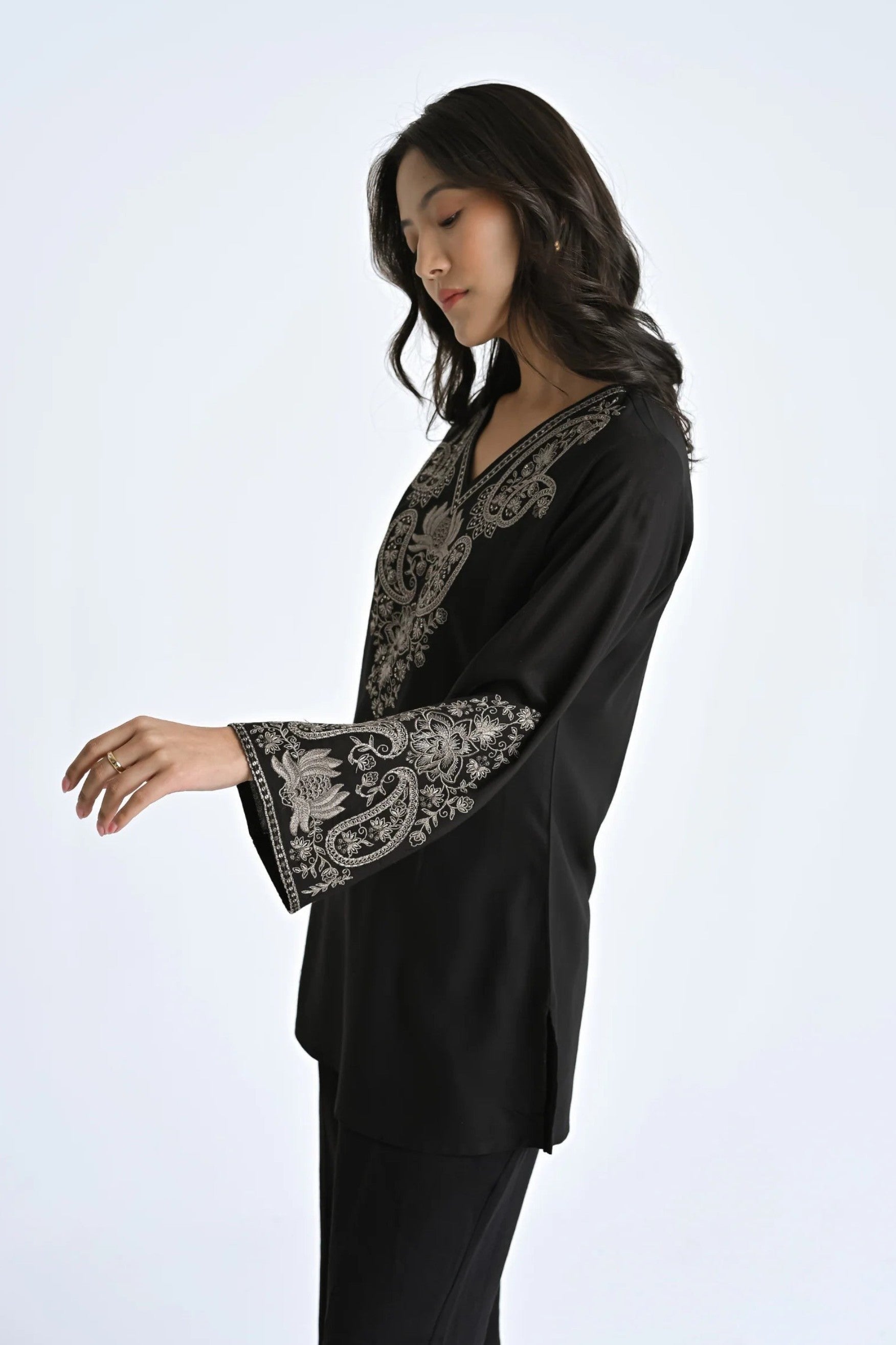 Model wearing an indigrey black Raya top with intricate white corded stem fill embroidery, V-neck, and flared sleeves.