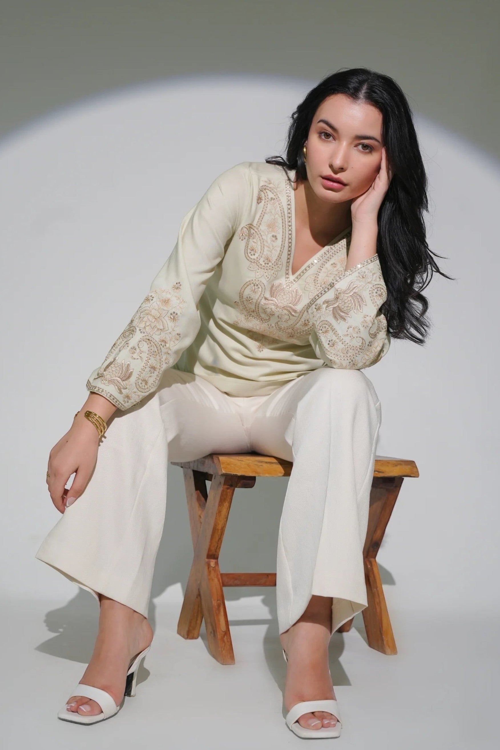Model wearing an ivory indigrey Raya top with tonal corded stem fill embroidery, V-neck, and flared sleeves.