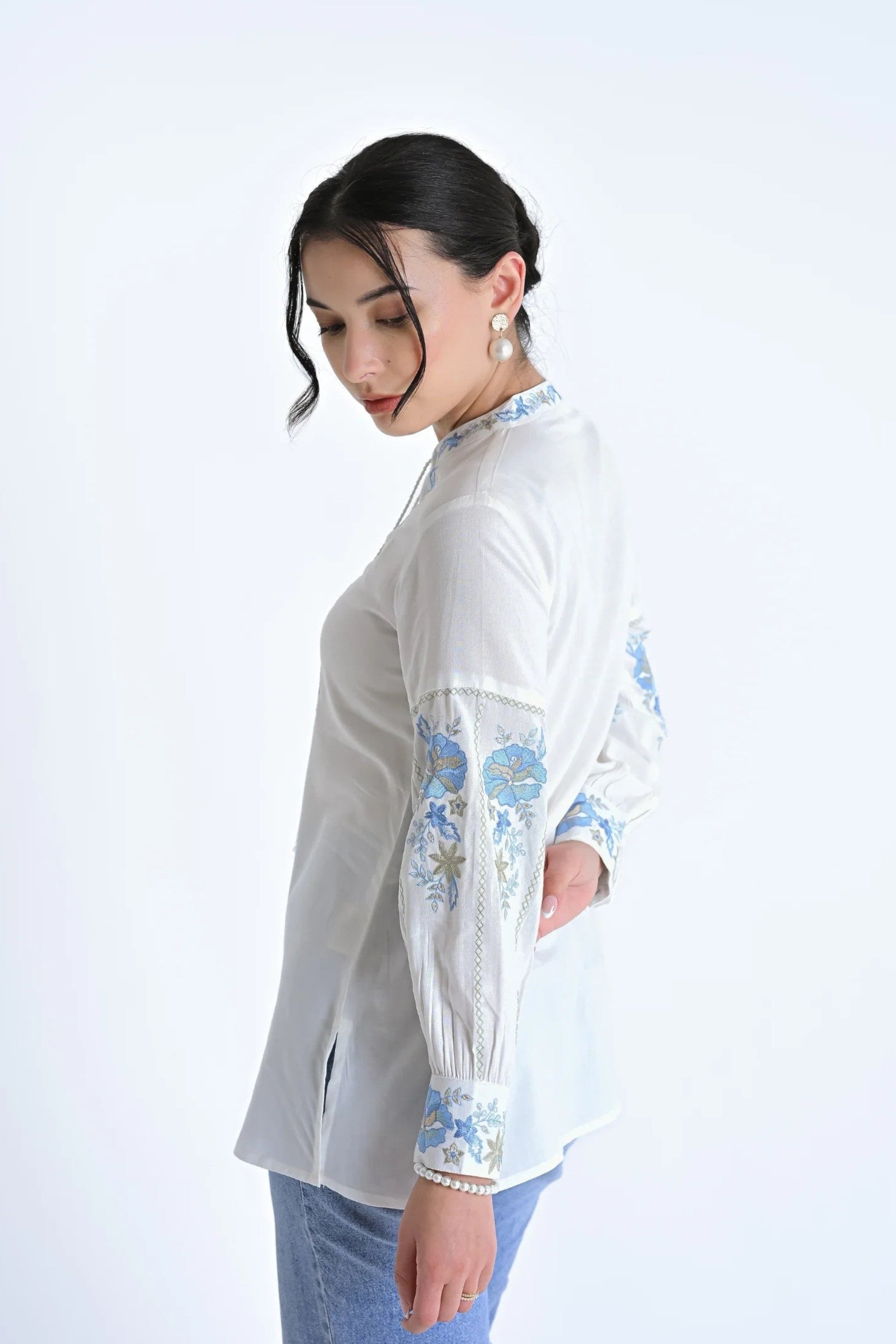 indigrey white shirt featuring blue floral Fly Brick stitch embroidery on sleeves and neckline with tassel details