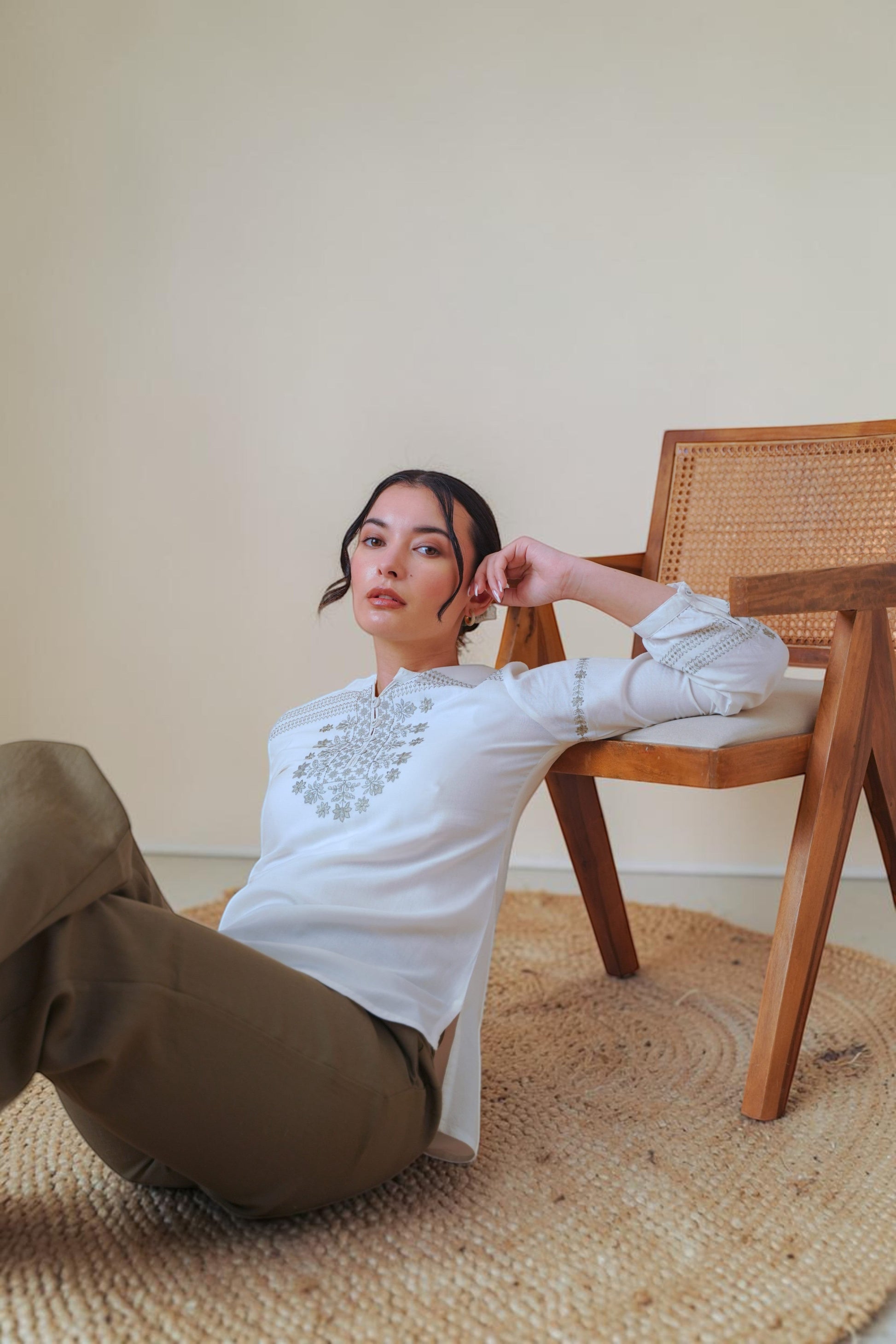 indigrey white long-sleeve top with intricate grey latticework embroidery, worn by a model sitting on a wooden chair.