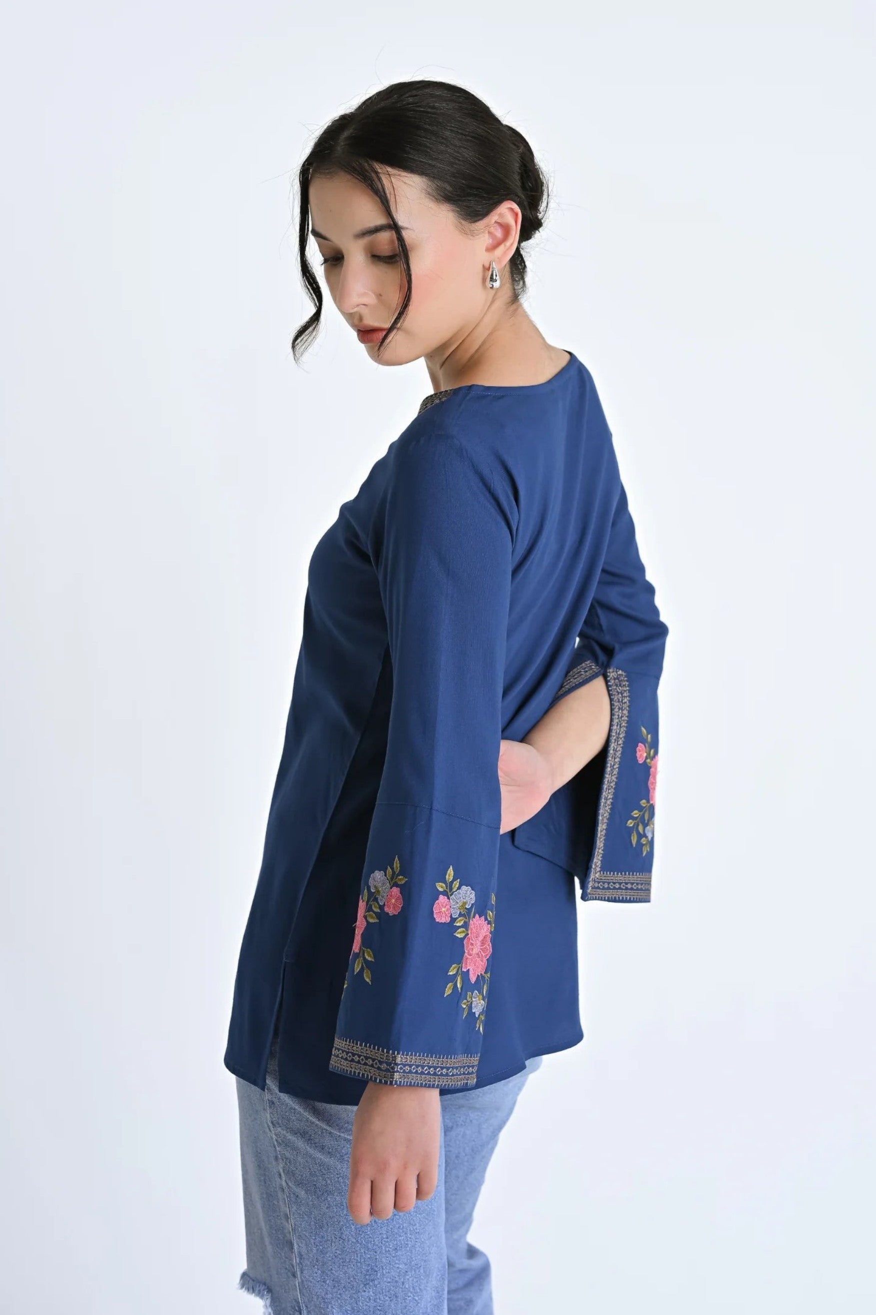 indigrey Zuri deep teal bell sleeve top with floral Sketchfill Cord embroidery on sleeves, worn by a woman.